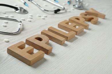 Photo of Word Epilepsy made of wooden letters, stethoscopes, pills and syringes on white table, closeup