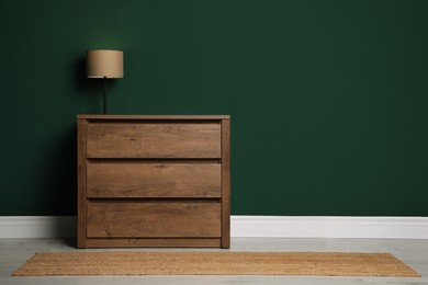 Modern wooden chest of drawers with lamp near green wall indoors. Space for text