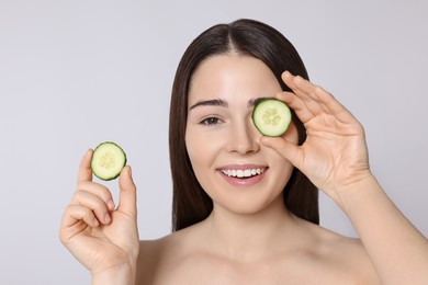 Photo of Woman holding pieces of cucumber on light grey background. Spa treatment