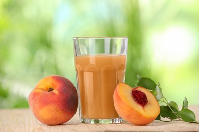 Photo of Tasty peach juice, fresh fruits and green leaves on wooden table outdoors