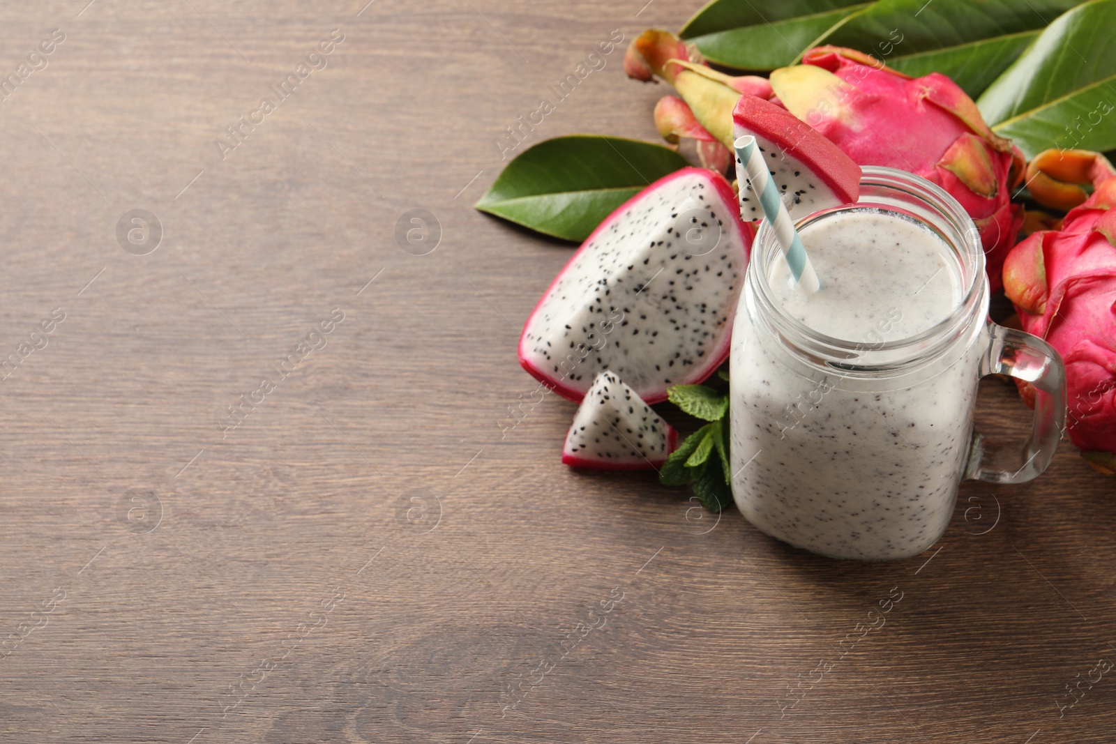 Photo of Delicious pitahaya smoothie in mason jar and fresh fruits on wooden table, space for text