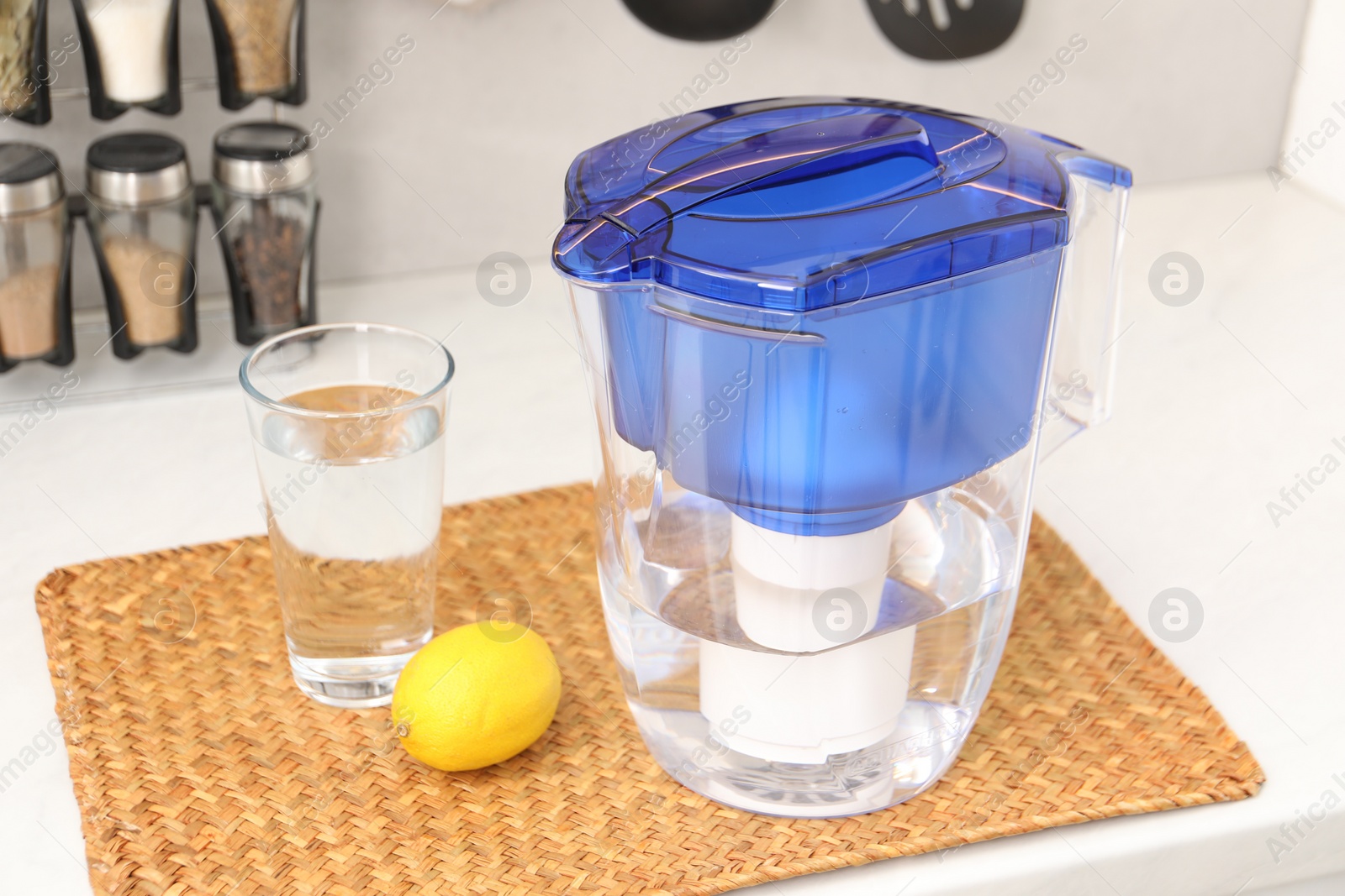 Photo of Water filter jug, glass and lemon on white countertop in kitchen