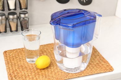 Photo of Water filter jug, glass and lemon on white countertop in kitchen