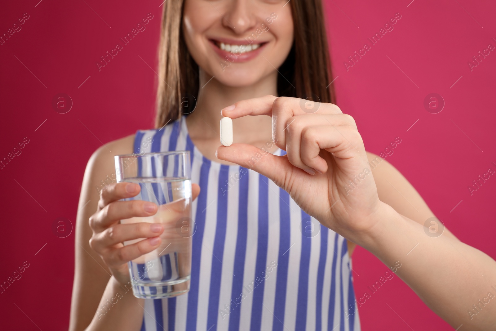 Photo of Young woman with vitamin pill and glass of water on pink background, closeup