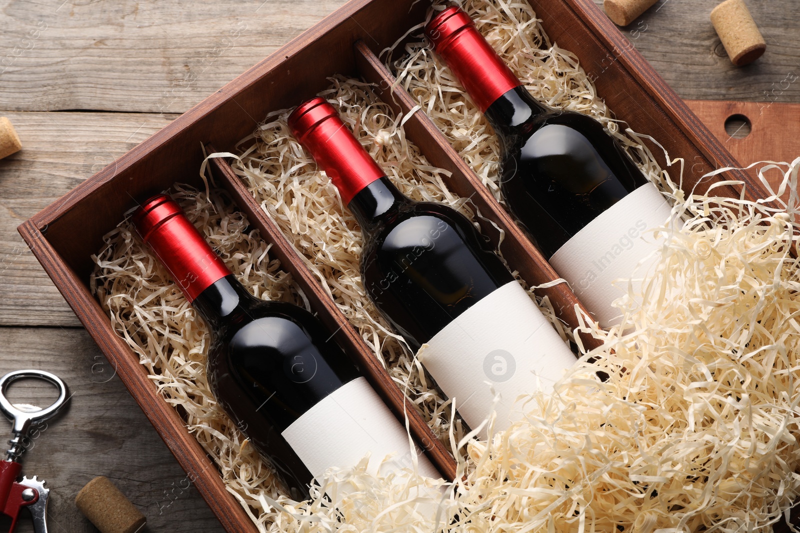 Photo of Box with wine bottles, corkscrew and corks on wooden table, flat lay