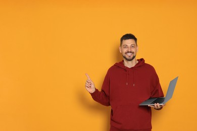 Photo of Happy man with laptop on orange background. Space for text