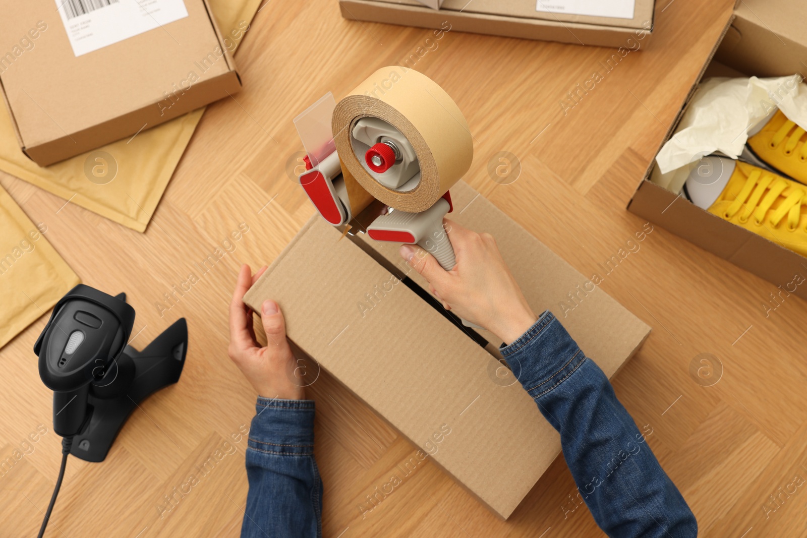 Photo of Woman taping parcel at wooden table in office, top view. Online store