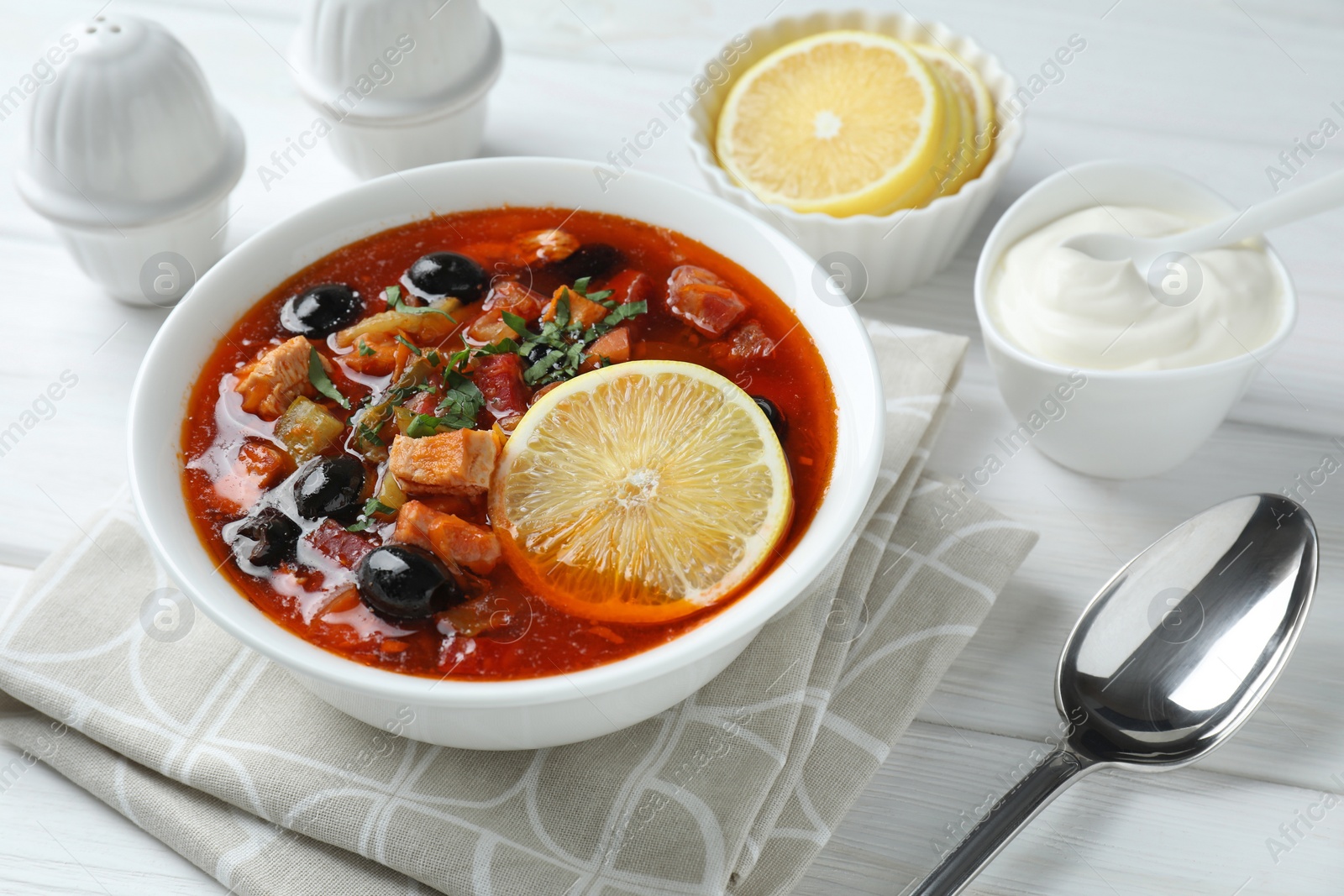 Photo of Meat solyanka soup with sausages, olives and vegetables served on white wooden table