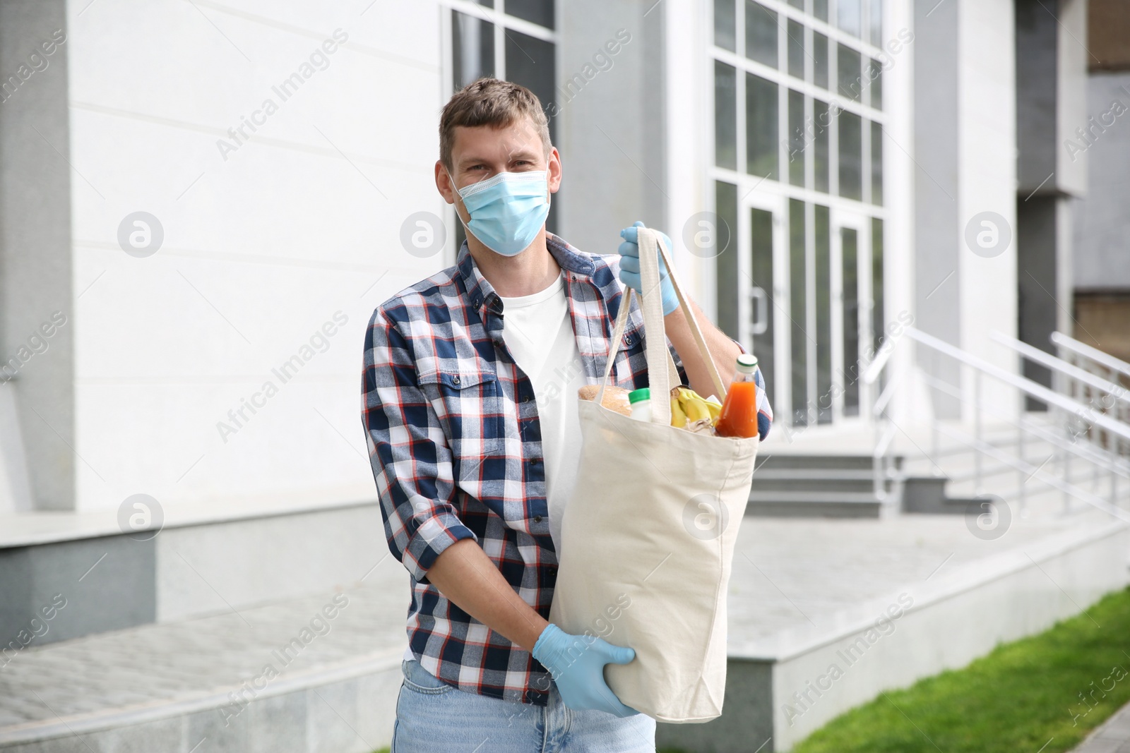 Photo of Male volunteer in protective mask and gloves with products on city street. Aid during coronavirus quarantine