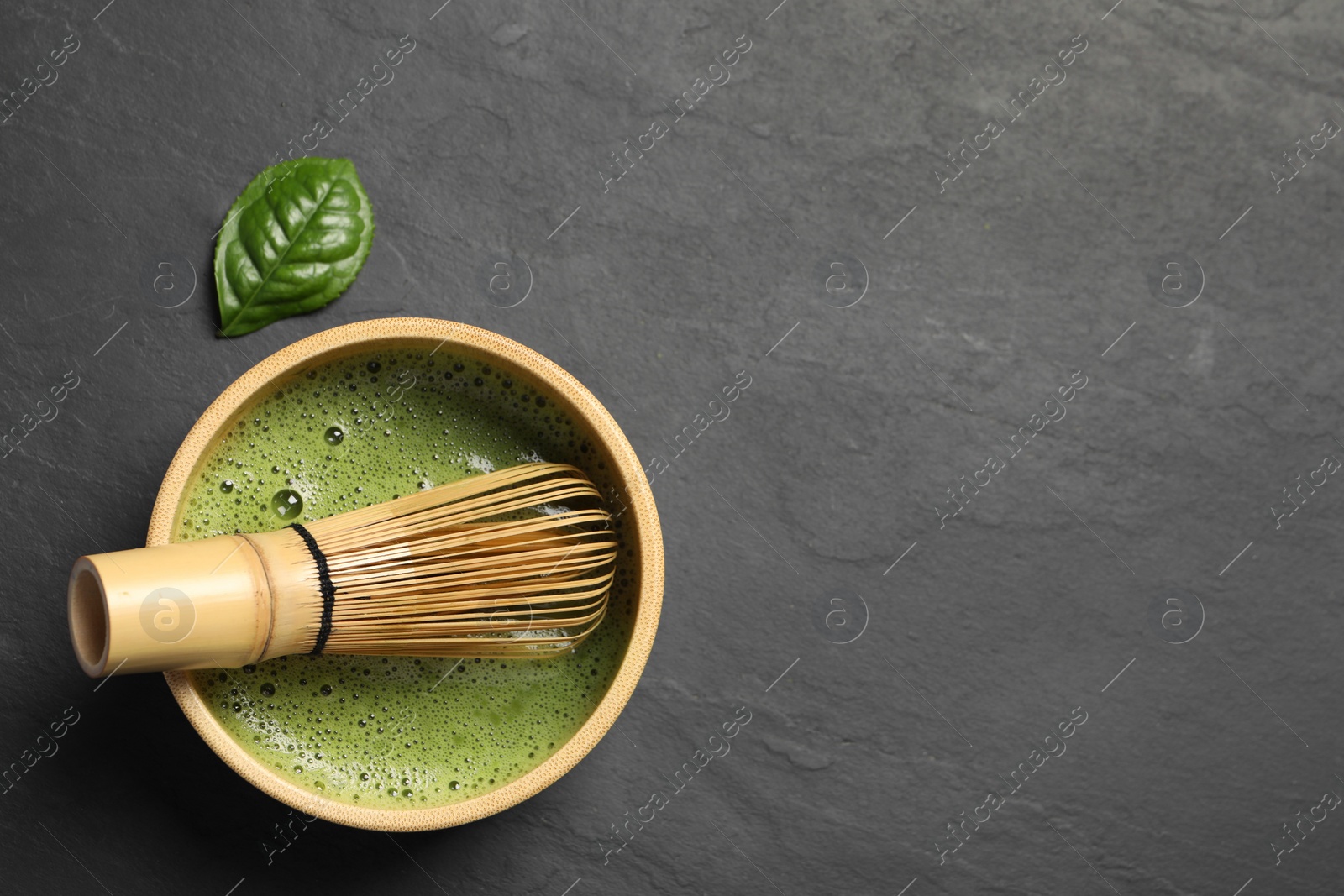 Photo of Cup of fresh matcha tea with bamboo whisk on black table, flat lay. Space for text