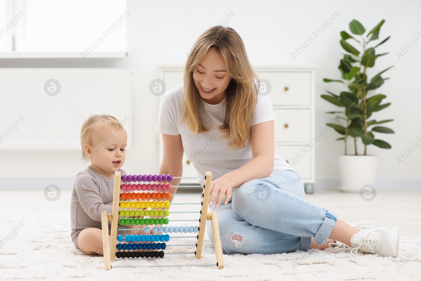 Photo of Children toys. Happy mother and her little son playing with wooden abacus on rug at home