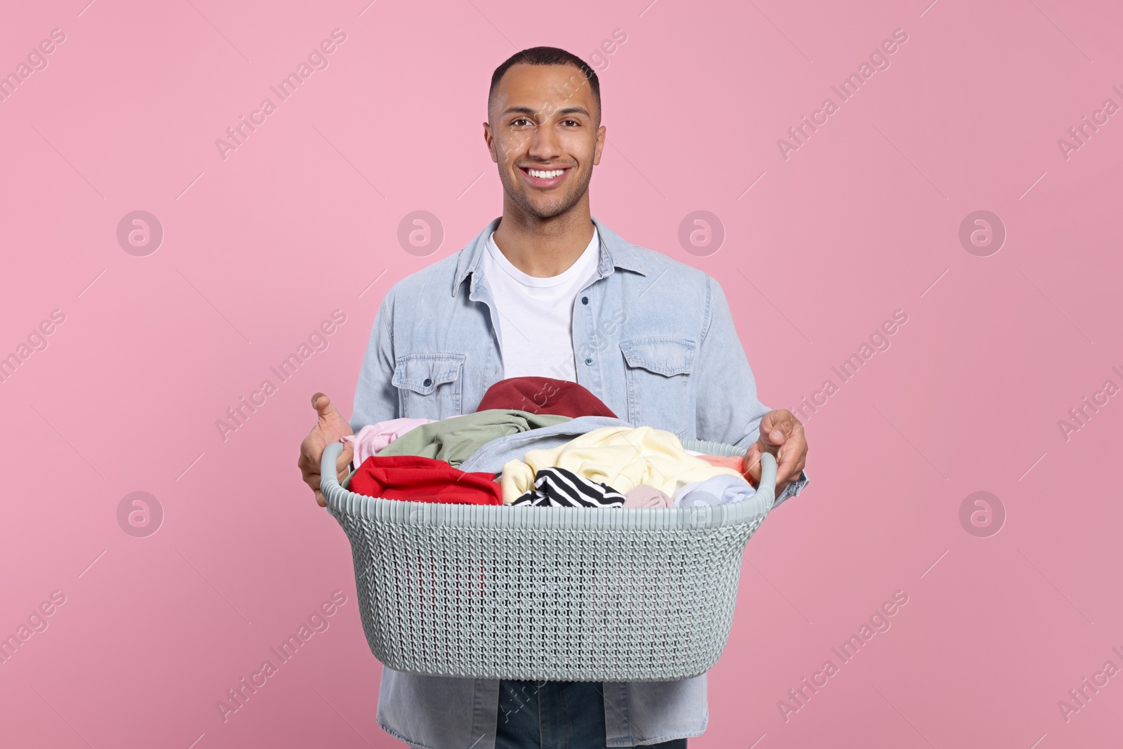 Photo of Happy man with basket full of laundry on pink background