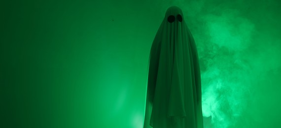 Photo of Creepy ghost. Woman covered with sheet in green light, space for text