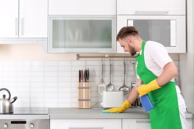 Photo of Young man in uniform cleaning kitchen counter