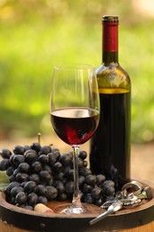 Photo of Delicious wine and ripe grapes on wooden barrel outdoors, closeup