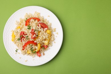 Photo of Plate of cooked bulgur with vegetables on light green table, top view. Space for text