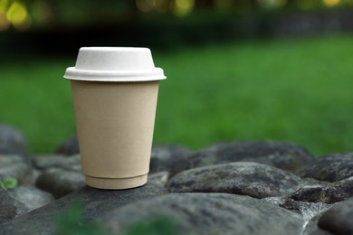 Photo of Cardboard takeaway coffee cup with lid on stones outdoors, space for text