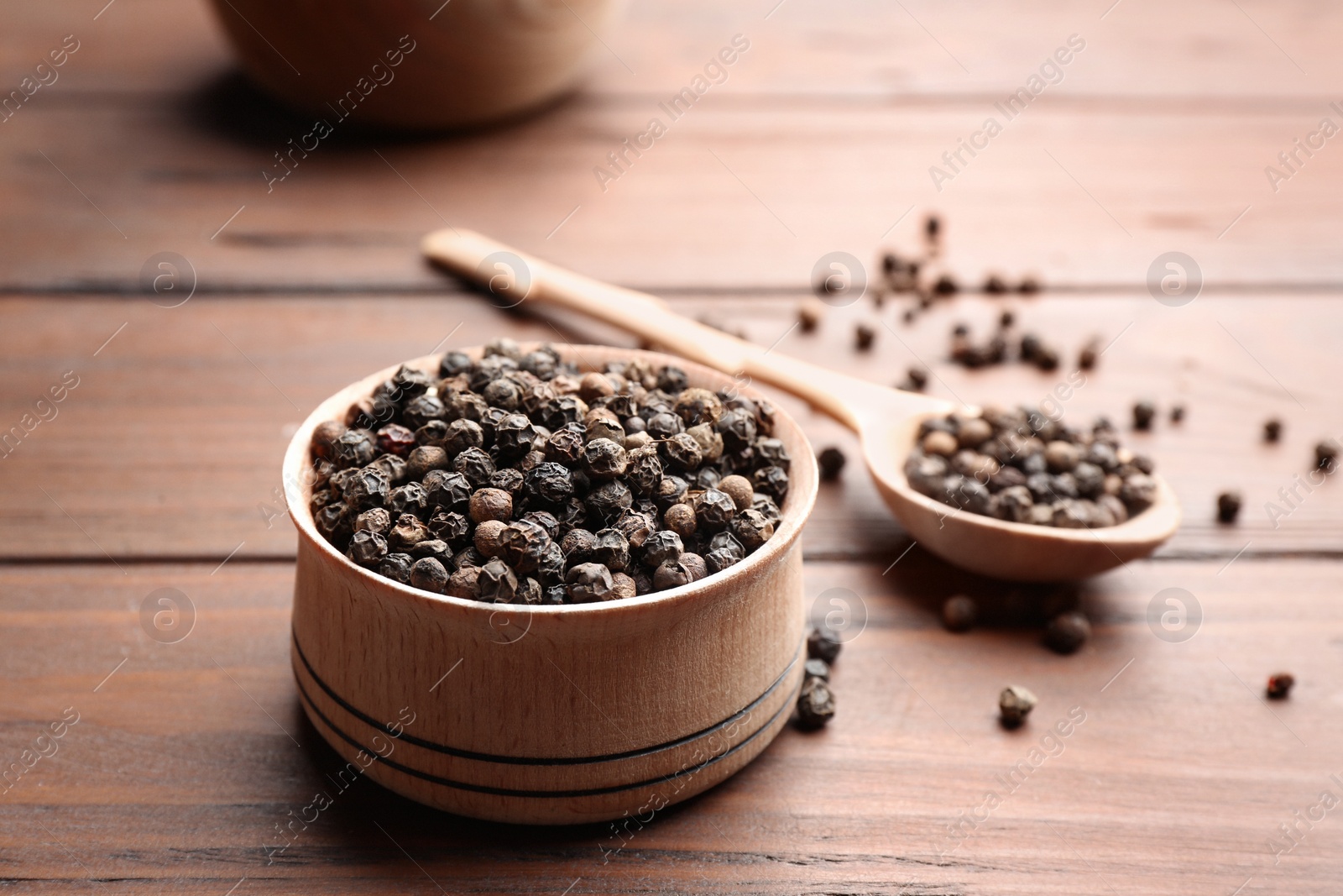 Photo of Bowl of black pepper corns and spoon on wooden table, space for text