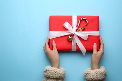 Woman holding red Christmas gift box on light blue background, top view