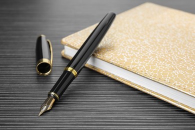 Stylish fountain pen and notebook on black wooden table, closeup