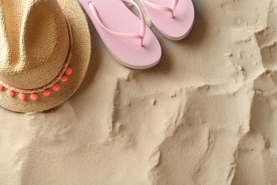 Straw hat and flip flops on sand, flat lay. Space for text