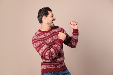 Happy young man in Christmas sweater on beige background