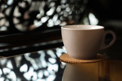 Photo of Cup with cork coaster on black table in cafe, closeup. Space for text