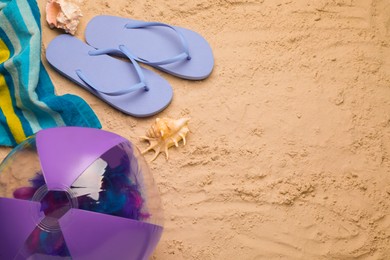 Photo of Bright beach ball, blanket, flip flops and shells on sand, flat lay. Space for text