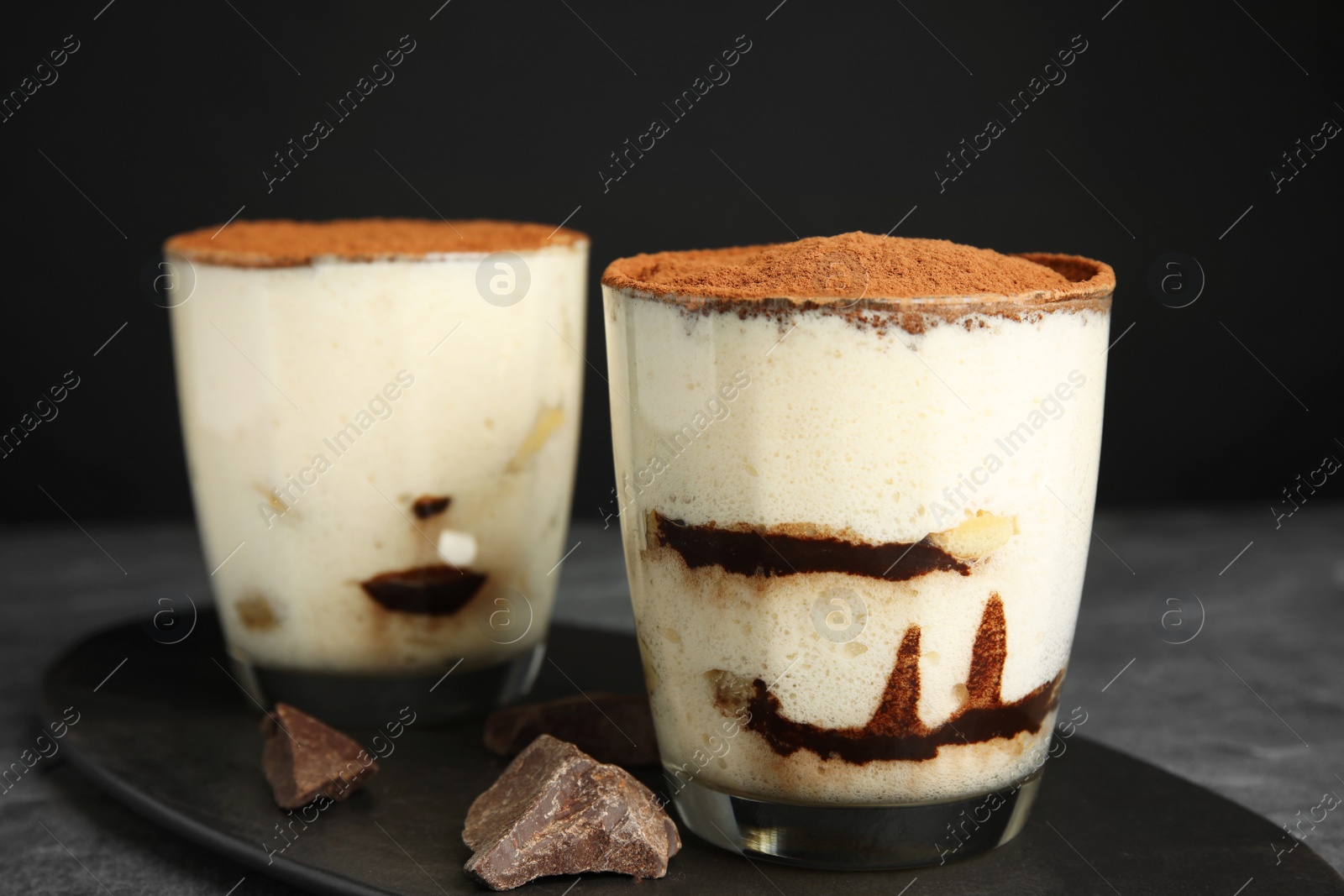 Photo of Two glasses of tiramisu cake on table against dark background, closeup