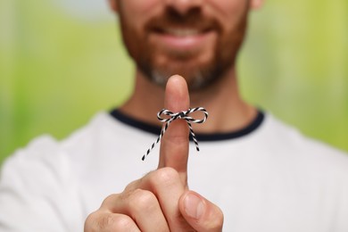 Photo of Man showing index finger with tied bow as reminder against green blurred background, focus on hand