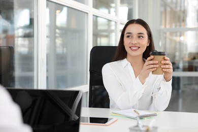 Photo of Happy woman with paper cup of coffee at desk in open plan office