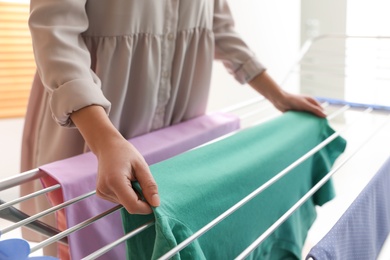 Photo of Young woman hanging clean laundry on drying rack at home, closeup