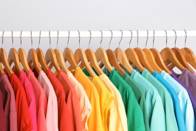 Photo of Rack with rainbow clothes on light background