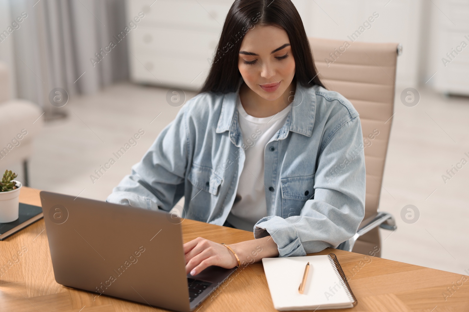 Photo of Young woman watching webinar at table in room