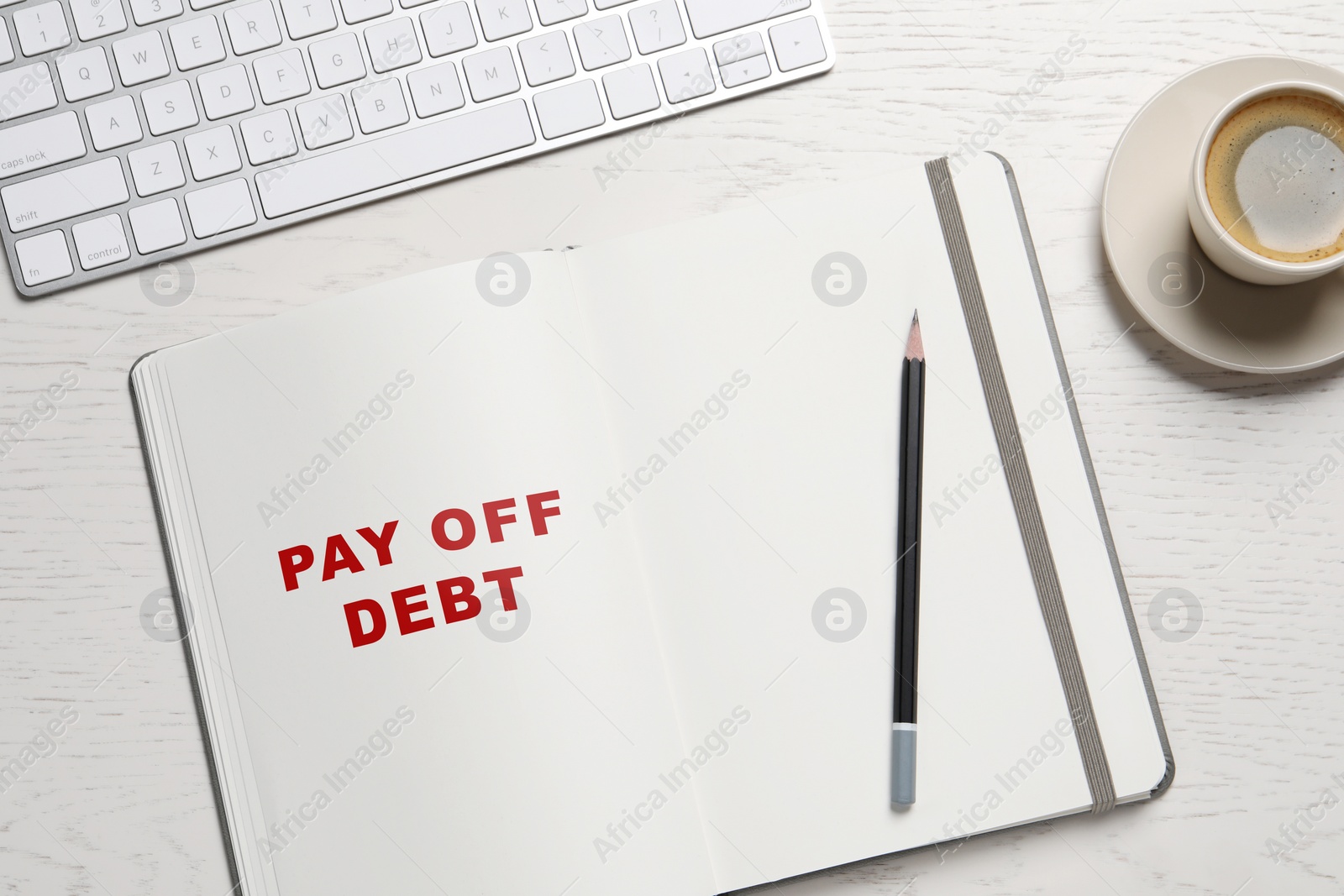 Image of Notebook with phrase Pay Off Debt, pencil, coffee and keyboard on white wooden table, flat lay