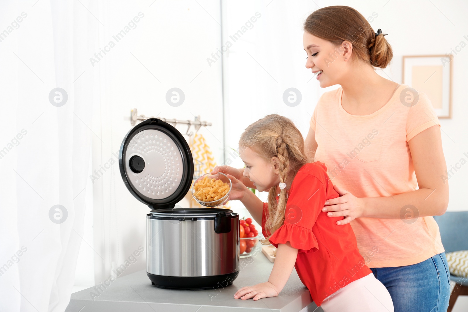 Photo of Mother and daughter preparing pasta with modern multi cooker in kitchen