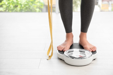 Woman with tape standing on scales indoors, space for text. Overweight problem