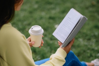 Photo of Young woman with cup of coffee reading book in park, closeup
