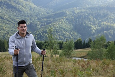 Photo of Tourist with trekking poles hiking through mountains, space for text