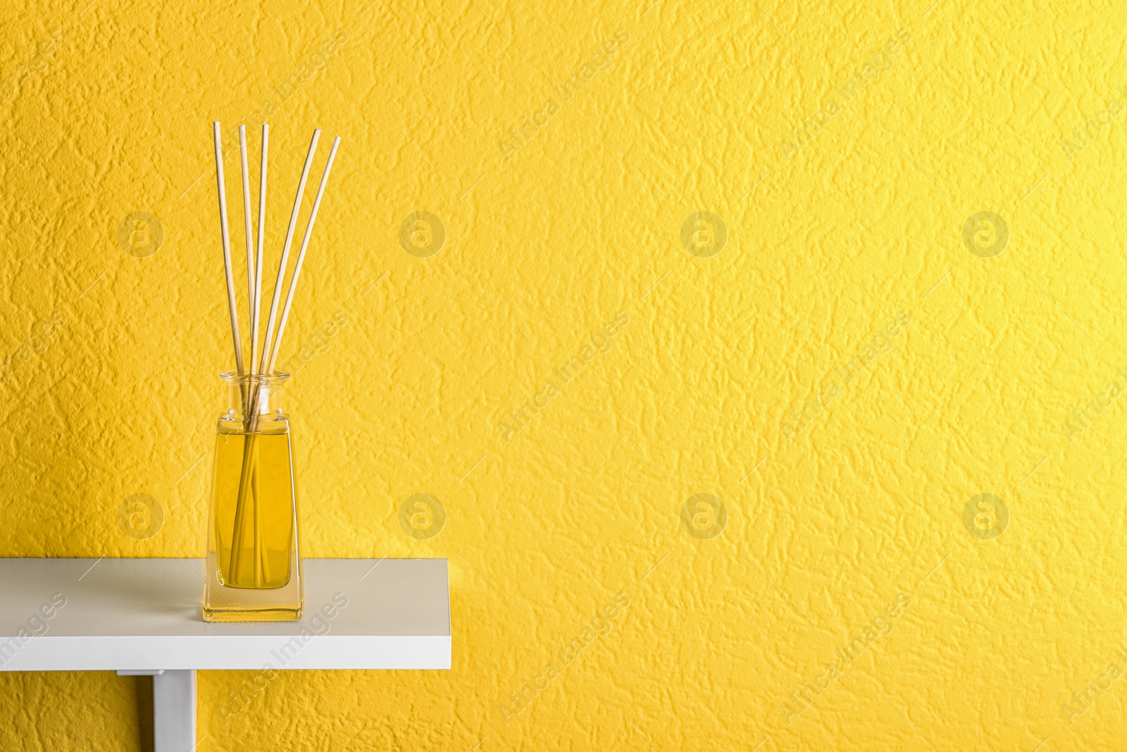Photo of Reed air freshener on table against yellow background, space for text