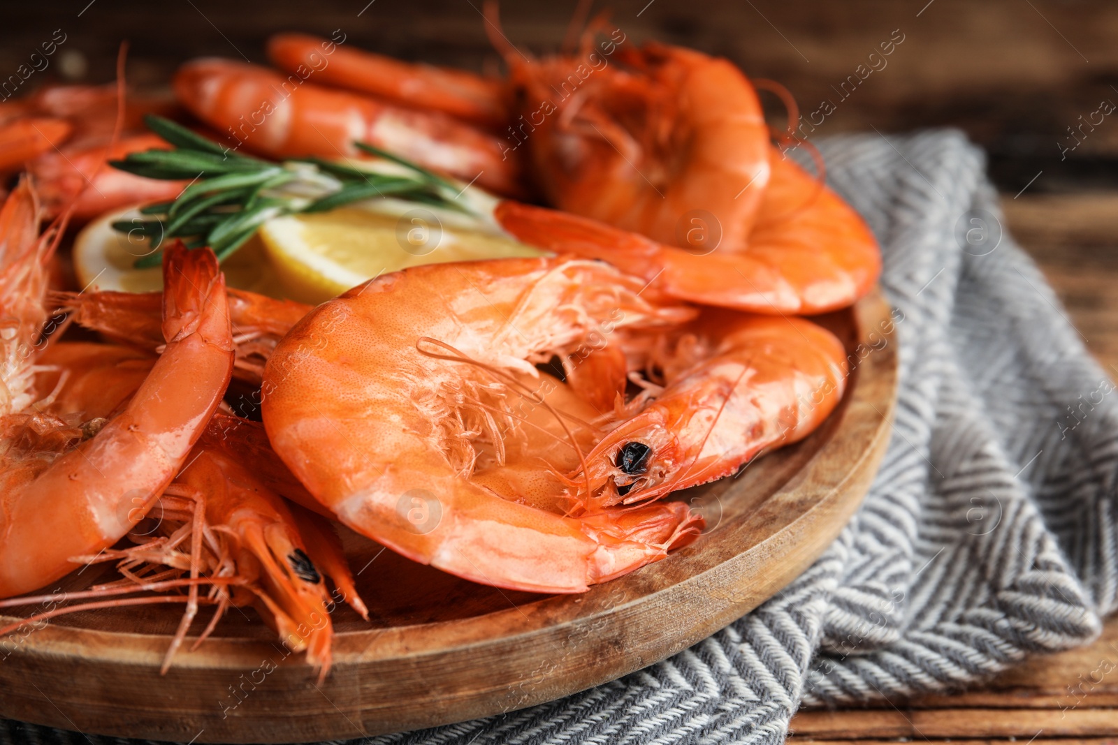 Photo of Delicious cooked shrimps with rosemary and lemon on wooden plate, closeup