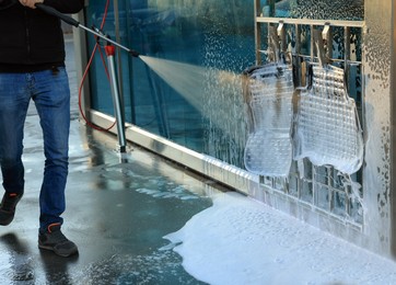 Photo of Man cleaning auto mats with high pressure water jet at self-service car wash, closeup