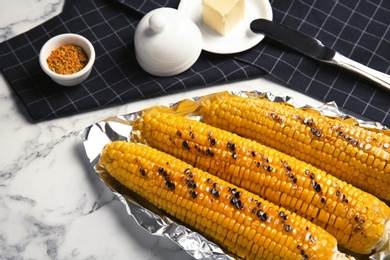 Photo of Fresh grilled tasty corn cobs served with butter on marble table