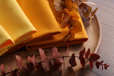 Tray with different kitchen napkins and decorative dry leaves on wooden table, closeup