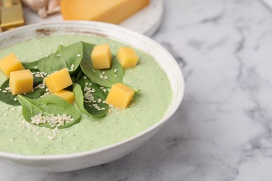 Delicious spinach cream soup with cheese and sesame seeds in bowl on white marble table, closeup. Space for text