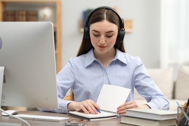 Photo of E-learning. Young woman taking notes during online lesson at table indoors