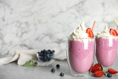 Tasty milk shakes with berries on grey marble table. Space for text