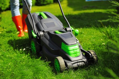 Photo of Woman cutting grass with lawn mower in garden on sunny day, closeup