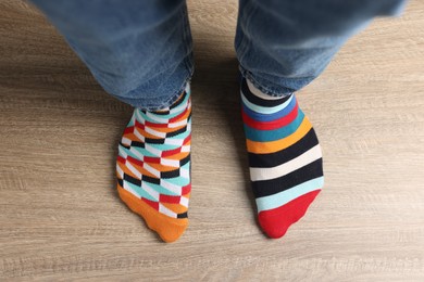 Man in different stylish socks standing on wooden floor, top view