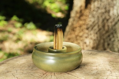 Smoldering palo santo stick in holder on wooden stump outdoors